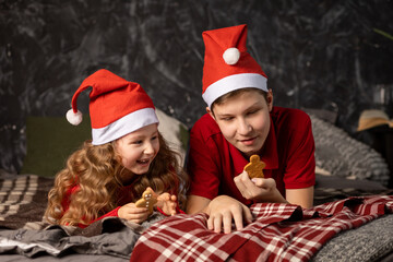 happy kids eating christmas gingerbread cookies in red santa hats. fun boy and girl play, laugh and smile for new year.