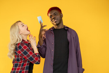 Couple budget. Greedy shopaholic. Family income. Gold digger. Multicultural pair of excited white woman begging for credit card money to Afro man isolated on orange free space.