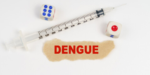 On a white surface lies a syringe, dice and a piece of paper with the inscription - DENGUE