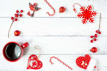 A mug with black coffee and New Year's decorations in red are around the perimeter against a light wooden background. Free space for text. View from the top point.