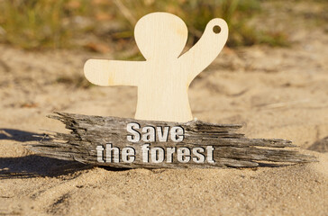 On the sand near the wooden figurine of a man there is a piece of wood with the inscription - Save the forest