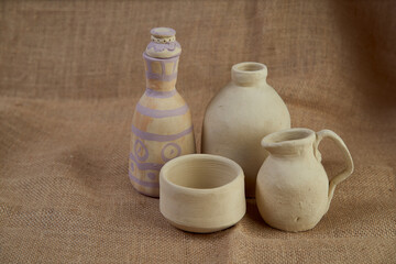 Crafts made of clay. Small chicken, cup and bottle on a background of burlap