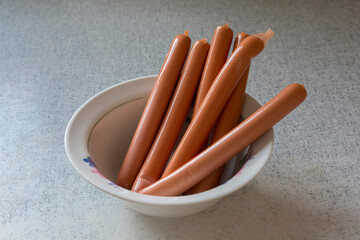 many meat sausages in cellulose packaging lie in a white plate