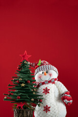Christmas background with pine tree and Snowman ornaments on red surface with copy space.
