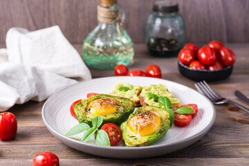 Hot appetizer baked avocado with egg, toast, cherry tomatoes and basil on a plate on a wooden table. Healthy eating. Flexitarian diet
