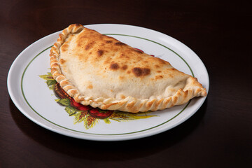 Closed calzone pizza on a white dish on a dark background