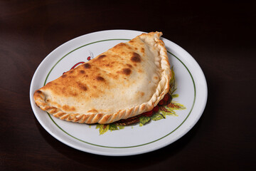 Closed calzone pizza on a white dish on a dark background