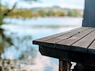 Eine braune Holzterasse und im Hintergrund der See und der Wald