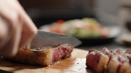 man slicing new york steak on olive wood board