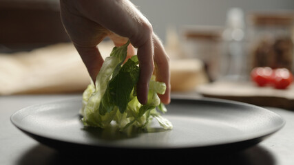 man hand put mixed greens on black plate closeup