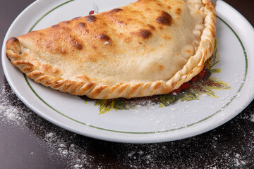 Closed calzone pizza on a white dish on a dark background