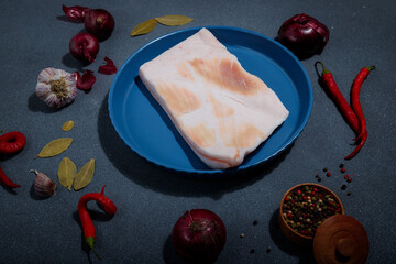 Piece of raw pork lard and ingredients for marinade: onions, garlic, red hot pepper, salt, bay leaf...