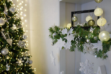 Christmas tree decorated with shiny garland and bulbs in white room. Festive vibes of winter...