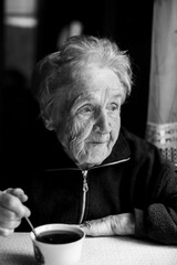 An old woman with a cup of tea. Black and white photo.