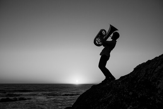 Silhouette of a man playing a trumpet by the ocean. Black and white photo.