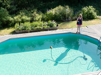 Young woman cleaning outdoor country pool. Outdoor pool in the backyard of the house.