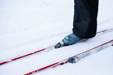 Man is skiing. Close-up of legs in gray ski boots on skis, man riding in snow on clear sunny day, side view. 