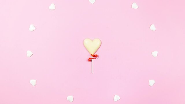 4k Two heart-shaped white chocolate candies are combined into one large, small hearts appear and disappear. Valentine's day concept. Flat lay. Copy space. Stop motion animation. Light pink background.