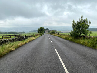 Fototapeta na wymiar Rainy weather over, Thick Hollins Road, with heavy cloud, fields, and trees near, Holmbridge, Holmfirth, UK