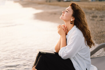 Woman closed her eyes, praying on a sea during beautiful sunset. Hands folded in prayer concept for...