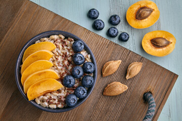 Whole grain oatmeal with apricot pieces and blueberries on a wooden tray