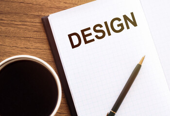 The word Design in a notebook on the office table next to glasses, a cup of coffee and a pencil