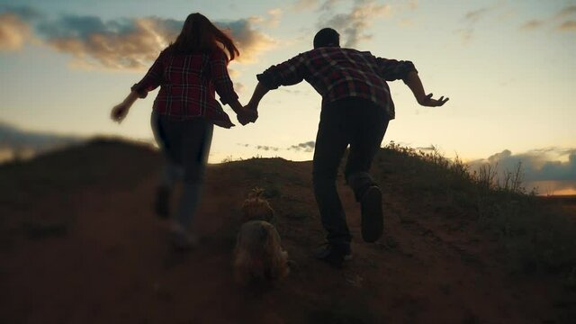 happy family couple and dog runs hands jumping up for joy at sunset on a hilltop and jumps. concept of team business concept travel freedom victory happiness teamwork. happy family parents hold hands