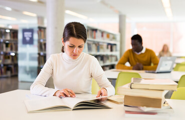 Portrait of confident woman with book in public library. High quality photo