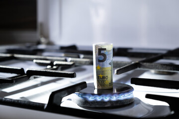 Concept of gas crisis. 5 euro bank note is burning on a kitchen stove. Cash money. High prices of...