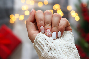 Idea of the winter manicure. Woman's hand with gel polish manicure white color and with snowflakes ornament against festive Christmas background. Selective focus