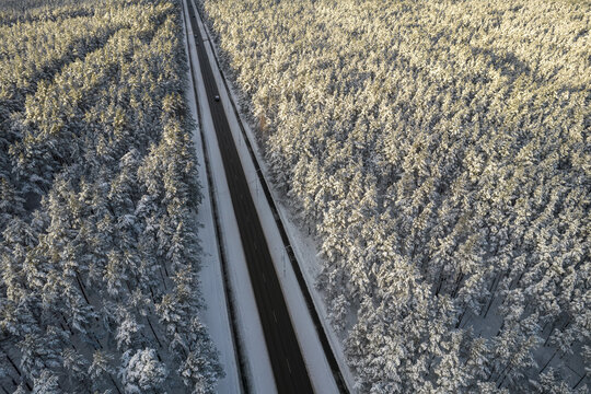 Aerial view of asphalt highway leading through frosty winter forests and groves covered with hoarfrost and snow. Drone photo of black road line and trees with chill snow in mountains. Christmas theme
