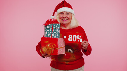 Grandmother woman showing gift boxes and 80 Percent discount inscriptions banner text. Christmas sweater. Black Friday. Advertising low prices shopping. Blue studio background. Happy New Year 2022