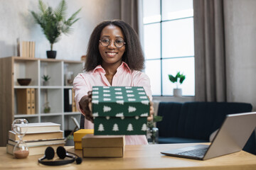 First person view of african female blogger opening gift boxes while sitting at home. Positive young woman doing live stream during unpacking process.
