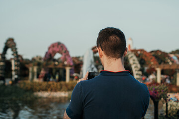 Young adult tourist with dark hair taking photos on his smartphone outdoor in the park at daytime