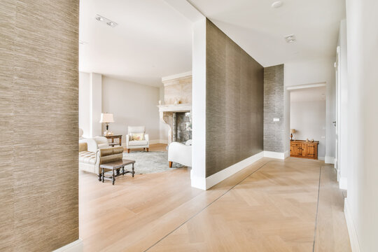 A wide corridor covered with brown wallpaper and an arch leading to the living room