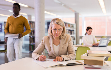 Fototapeta premium Woman with books sits at table in the library. High quality photo
