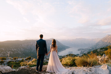 Fototapeta na wymiar Bride and groom stand on the top of the mountain and look into the valley. Back view
