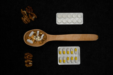 Medical pills and capsules in a wooden spoon. White tablets and capsules. Medicines and vitamins. Peeled walnut. Packing of tablets. Pharmacology. Healthy Eating. Photo on a dark background.