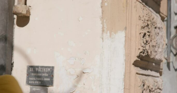 Male prostitute on the street answers something to client and with gesture of head shows to follow him. Stylish man in glasses with red lenses and yellow faux fur coat posing outdoor.