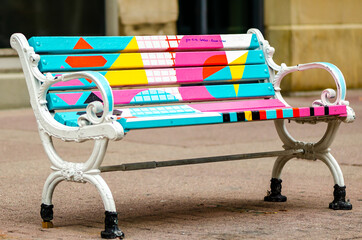 Old cast iron bench with colorful painted wooden slats and a hand note: give to the homeless,...