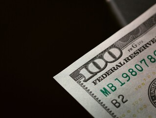 One hundred dollar bill. Focus on a corner, showing the number, with black negative space.