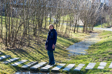 Outdoor portrait of a woman with a blue coat, a scarf and eyeglasses standing on a path in the wetland creek of a Brussels park