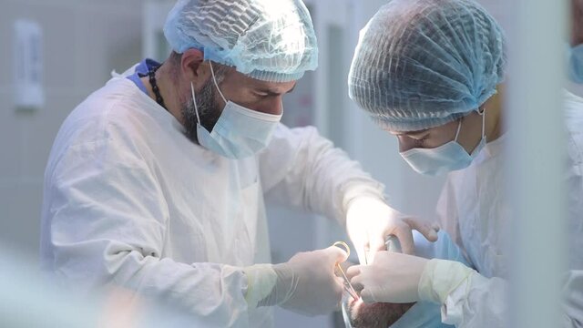 Surgeon and nurse during a dental operation.Anesthetized patient in the operating room.Installation of dental implants or tooth extraction in the clinic. General anesthesia during orthodontic surgery.