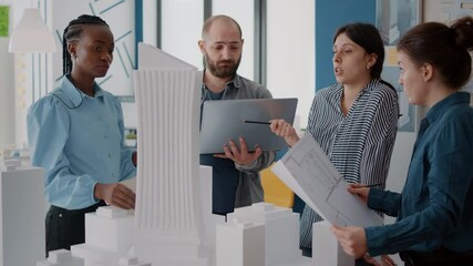 Colleagues working with laptop and blueprints to analyze building model in office. Workmates designing urban constructionwith laptop and maquette, doing teamwork for development.