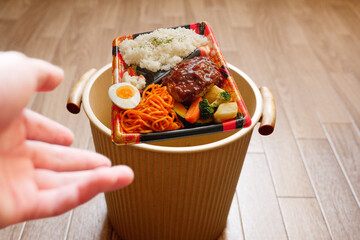 食品ロスのイメージで弁当をゴミ箱に投げ捨てる
