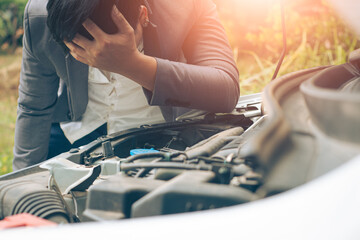 Business man using mobile phone while looking at broken down car on road.