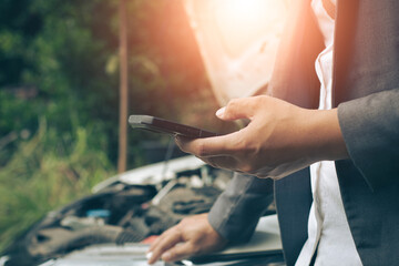 Business man using mobile phone while looking at broken down car on road.