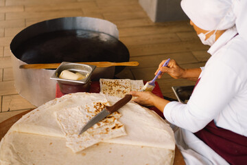 Turkish Woman making Tortillas on a wooden rustic table. A cook prepares tortillas with different fillings at a street in the summer.