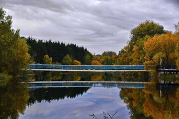 long metal bridge across the river with reflection in water on the background of an autumn landscape