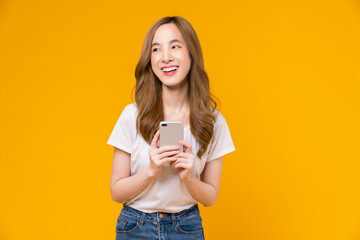 Beautiful Asian woman holding smartphone and smiling with typing on mobile, light yellow background.